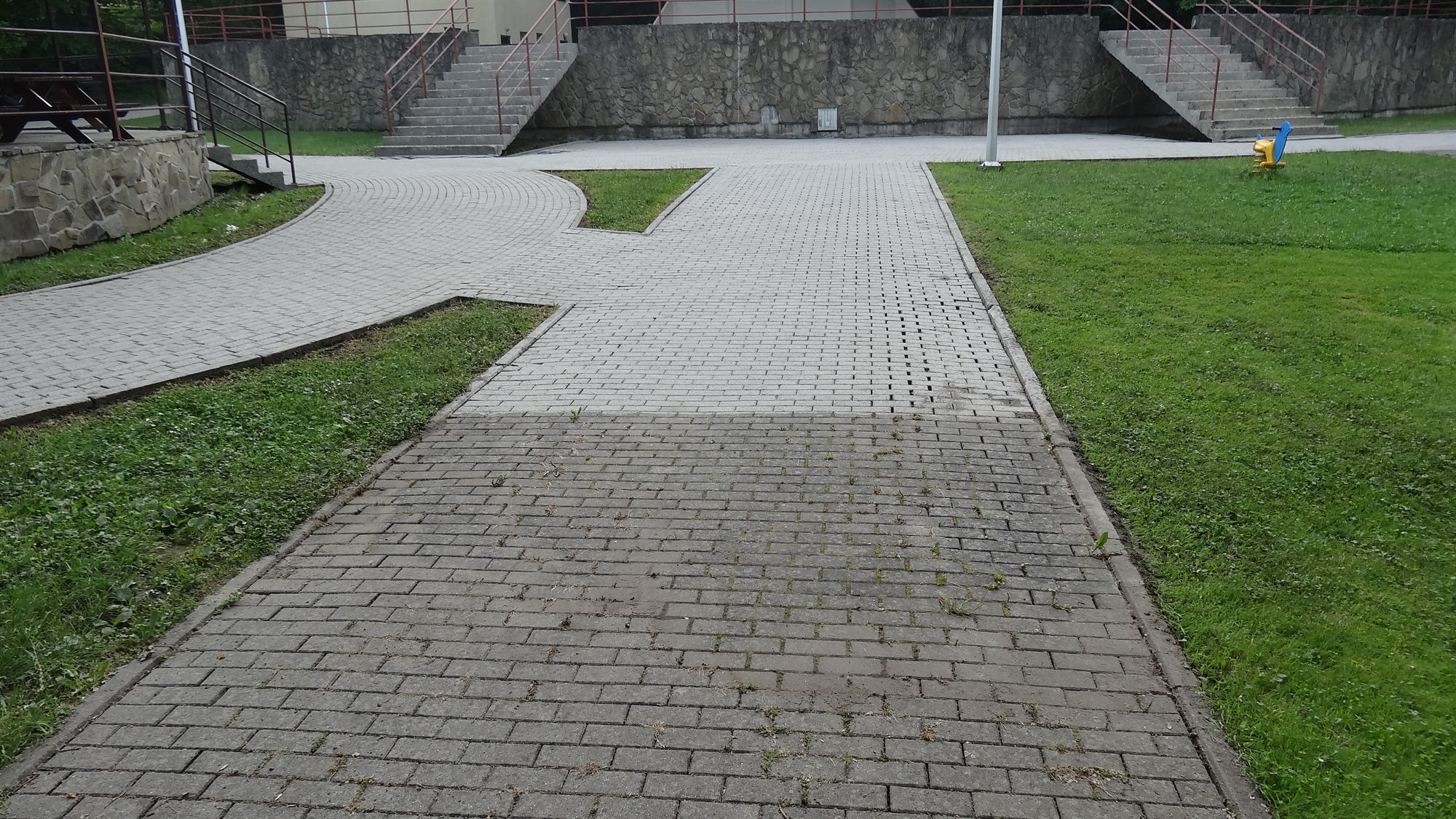 Podejście z kostki brukowej w trakcie czyszczenia, górna część już umyta, dolna wciąż z zaschniętym brudem i chwastami
