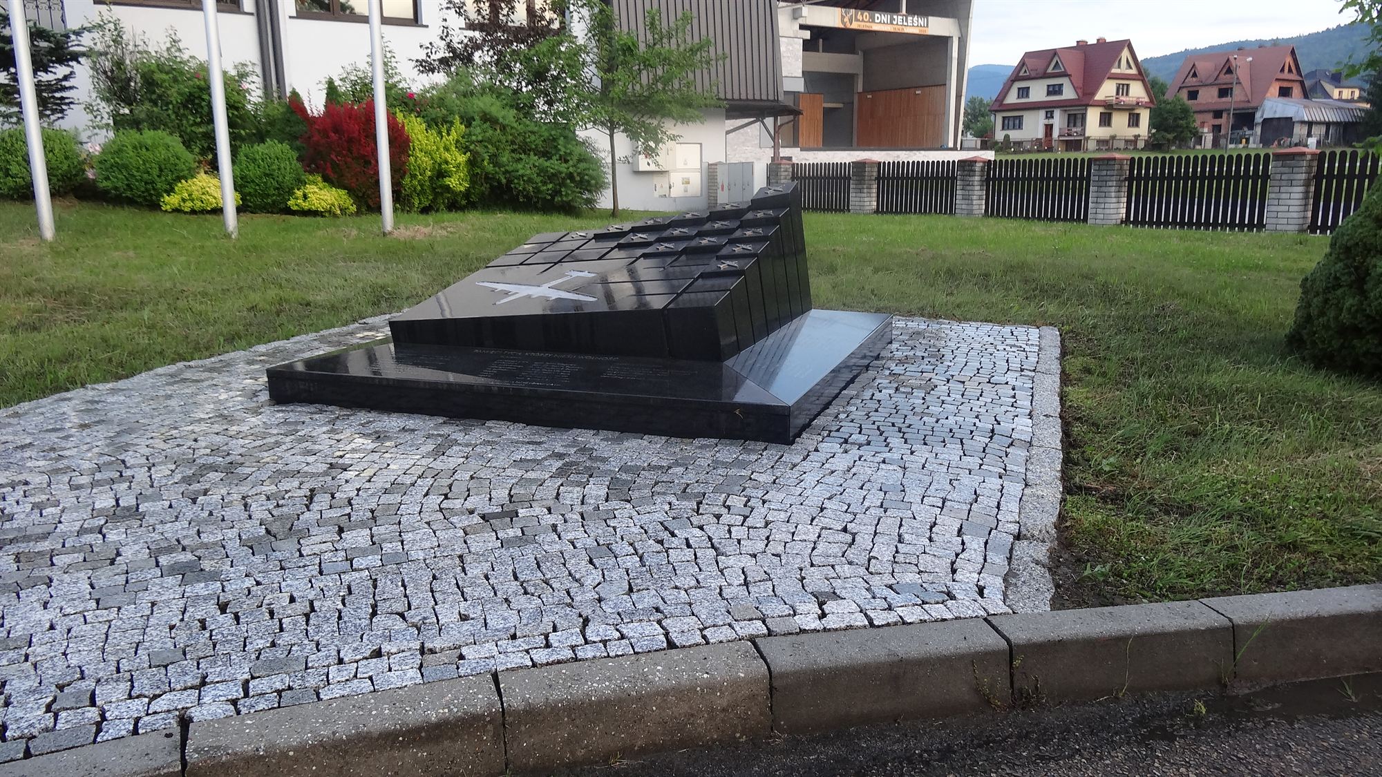 Plac z kostki granitowej wokół pomnika, w tle zabudowa i pasmo Beskidów